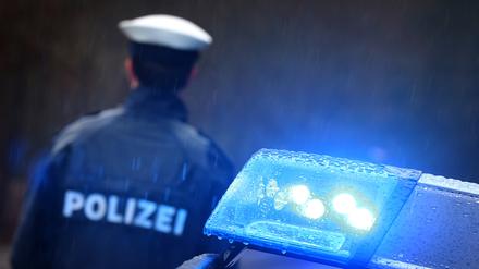 Ein Polizist steht im Regen vor einem Streifenwagen.