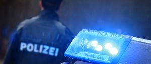Ein Polizist steht im Regen vor einem Streifenwagen.