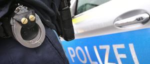 Ein Polizist mit Handschellen und einer Pistole am Gürtel steht vor einem Streifenwagen. (Symbolbild)