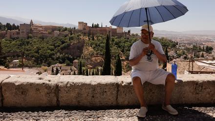 Ein Tourist sitzt mit einem Sonnenschirm auf einer Mauer in Granada. Hitzewellen gefährden den Tourismus in Spanien.