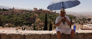 Ein Tourist sitzt mit einem Sonnenschirm auf einer Mauer in Granada. Hitzewellen gefährden den Tourismus in Spanien.