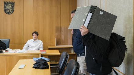 Der Angeklagte verdeckt vor Prozessauftakt sein Gesicht mit einem Aktenordner.  