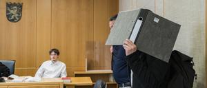 Der Angeklagte verdeckt vor Prozessauftakt sein Gesicht mit einem Aktenordner.  