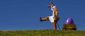 Ein lebensgroßer Osterhase freut sich über das kommende Osterfest, an seinem Leiterwagen präsentiert er bunte Ostereier in seinem Körbchen.