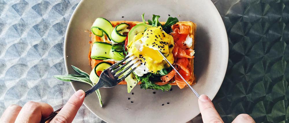 Eating brunch with waffle, avocado, cucumber, salmon and poached egg, personal perspective