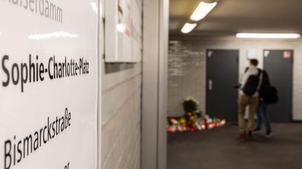 Menschen stehen im U-Bahnhof vor einer mit Blumen und Kerzen dekorierten Trauerstätte am Sophie-Charlotte-Platz. 