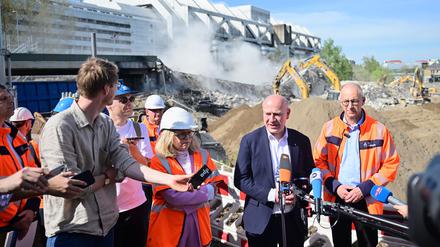 Während der Regierende Bürgermeister Kai Wegner mit Journalisten spricht, kracht das letzte Teilstück der maroden Brücke hinter ihm zu Boden. 