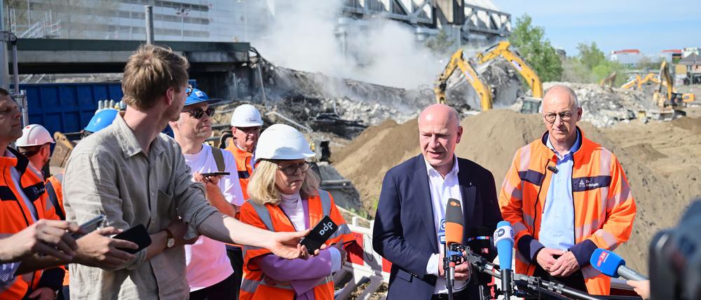 Während der Regierende Bürgermeister Kai Wegner mit Journalisten spricht, kracht das letzte Teilstück der maroden Brücke hinter ihm zu Boden.