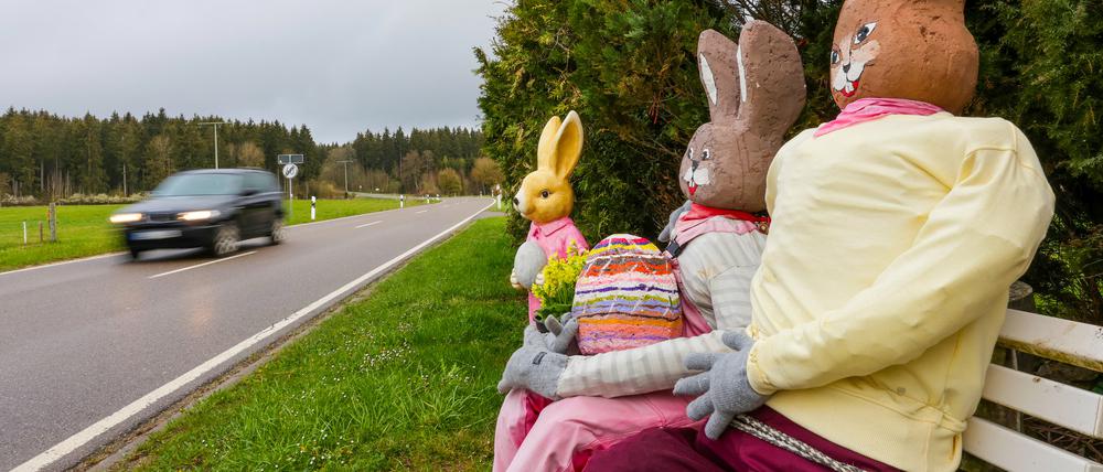 Mit Stroh ausgestopfte, selbstgebastelte Osterhasenfiguren sitzen an einer Landstraße.