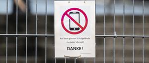 Ein Schild mit einem durchgestrichenen Smartphone und der Aufschrift «Auf dem ganzen Schulgelände - zu jeder Uhrzeit! DANKE!» hängt am Zugangstor zum Schulhof eines Gymnasiums und weist auf ein generelles Handyverbot hin. 