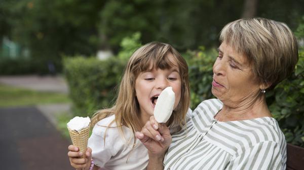 grandmother and child granddaughter eat ice cream in the park on a summer day. happy family has fun together in nature