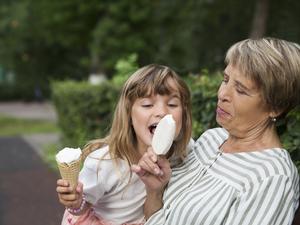 grandmother and child granddaughter eat ice cream in the park on a summer day. happy family has fun together in nature