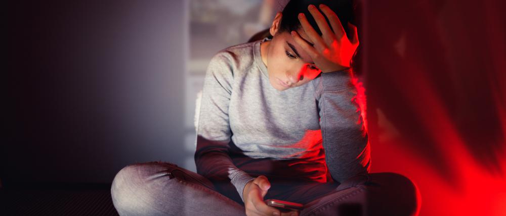 Eine 13-Jährige blickt in einem dunklen Raum auf ihr Smartphone. Über sie gelegt erscheint das Bild, das sie sich gerade ansieht.