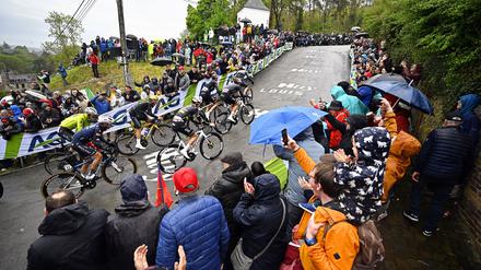 Olympiasieger Remco Evenepoel (M) mit goldenem Helm an der Mauer von Huy. Rechts neben ihm Tadej Pogacar.