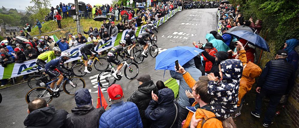 Olympiasieger Remco Evenepoel (M) mit goldenem Helm an der Mauer von Huy. Rechts neben ihm Tadej Pogacar.