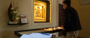 Ein Kondolenzbuch zum Tod von Papst Franziskus liegt in der Katholischen Probsteikirche St. Peter und Paul in Potsdam vor einem kleinen Foto des Papstes. Im Hintergrund hat ein junger Mann eine Kerze angezündet.