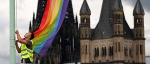 Ein Arbeiter hängt nach der Entscheidung im Bundestag über die „Ehe für alle“ vor der Kulisse des Doms in Köln eine Regenbogenfahne auf.