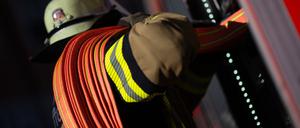 Eine Einsatzkraft der Feuerwehr nimmt einen Schlauch aus einem Einsatzfahrzeug der Feuerwehr. (Symbolbild)