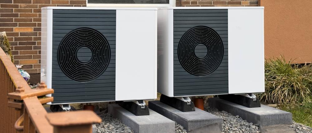 Zwei Wärmepumpen werden an einem Mehrfamilienhaus in einem Vorgarten montiert.
