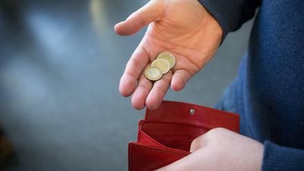 Münzen im Wert von fünf Euro werden in Paderborn über ein rotes Portemonnaie gehalten.  