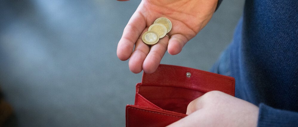 ARCHIV - 31.01.2017, Nordrhein-Westfalen, Paderborn: ILLUSTRATION - Münzen im Wert von fünf Euro werden in Paderborn über ein rotes Portemonnaie gehalten. (zu dpa: «Wohlfahrtsverband: Jeder Sechste in MV ist arm») Foto: Friso Gentsch/dpa +++ dpa-Bildfunk +++