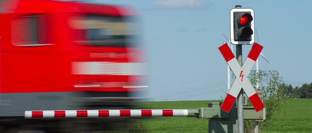 Ein Zug fährt an einem geschlossenem Bahnübergang vorbei.  