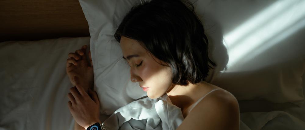 Eine Frau liegt mit ihrer Smartwatch am Arm im Bett.