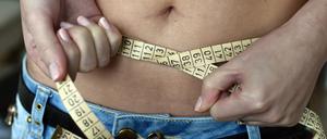 Eine junge Frau legt ein Maßband um ihren Bauch. 