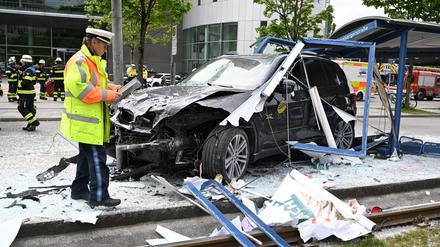 München: Ein Polizist steht neben dem Unfallfahrzeug in den Glassplittern einer Haltestelle. Ein Auto fährt in der Münchner Innenstadt in eine Haltestelle. Mehrere Menschen werden verletzt, drei von ihnen schwer. Der Rettungsdienst ist im Großeinsatz.