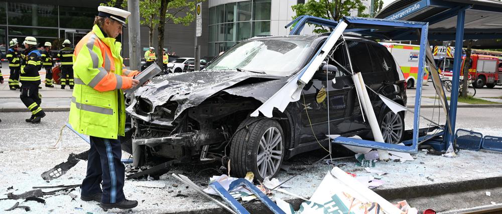 München: Ein Polizist steht neben dem Unfallfahrzeug in den Glassplittern einer Haltestelle. Ein Auto fährt in der Münchner Innenstadt in eine Haltestelle. Mehrere Menschen werden verletzt, drei von ihnen schwer. Der Rettungsdienst ist im Großeinsatz.