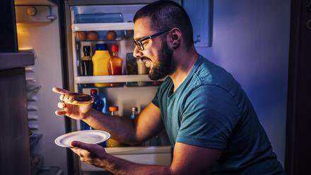 Ein Mann nimmt sich einen Mitternachtssnack aus dem Kühlschrank.