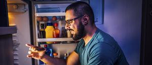 Ein Mann nimmt sich einen Mitternachtssnack aus dem Kühlschrank.