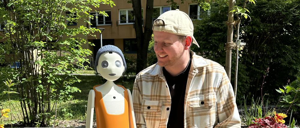 Tom Hettinger von der Sozialstiftung Köpenick sitzt mit Willi im Garten des Pflegeheims.