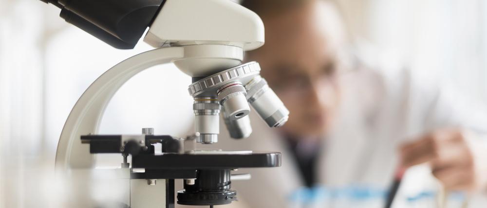 Ein Forscher vor einem Mikroskop. In den USA wird derzeit auch biomedizinische Forschung von Trumps Kürzungen eingeschränkt.