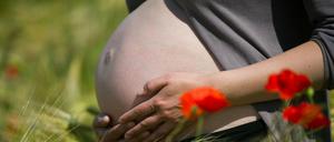 Eine im neunten Monat schwangere Frau steht in einem Getreidefeld mit Mohnblumen.
