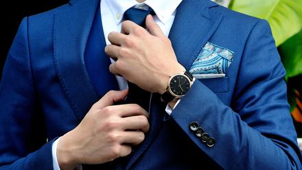 Ein Man im blauen Anzug und Einstecktuch rückt sich den Krawattenknoten zurecht.