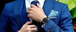 Ein Man im blauen Anzug und Einstecktuch rückt sich den Krawattenknoten zurecht.