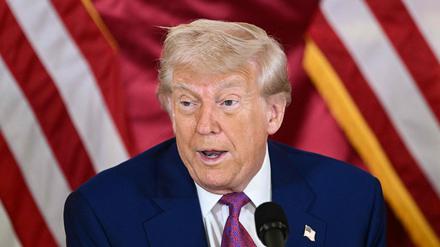 Donald Trump ist vor zwei US-amerikanischen Flaggen vor einem Mikrofon zu sehen.
