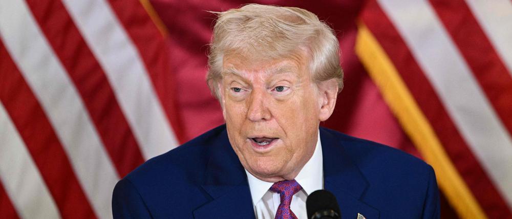 Donald Trump ist vor zwei US-amerikanischen Flaggen vor einem Mikrofon zu sehen.