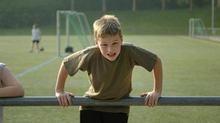 Junge stemmt sich auf einem Fußballplatz an einem Geländer hoch.