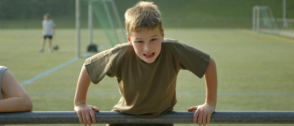 Junge stemmt sich auf einem Fußballplatz an einem Geländer hoch.