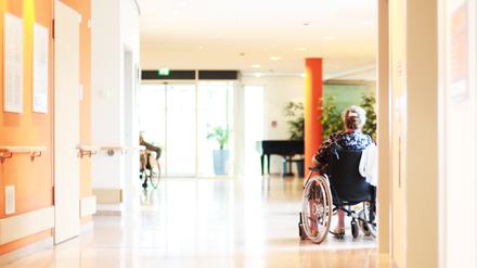 Eine Frau sitzt im Rollstuhl auf dem Flur eines Pflegeheims.