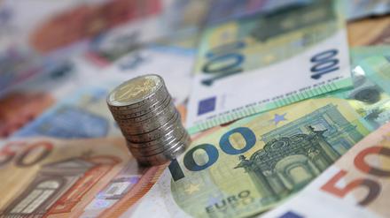Ein Stapel mit Zwei-Euro-Münzen steht auf verschiedenen Euro-Banknoten.
