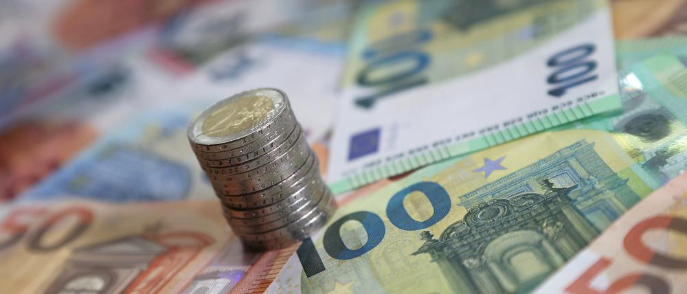 Ein Stapel mit Zwei-Euro-Münzen steht auf verschiedenen Euro-Banknoten.