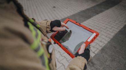 Eine Einsatzkraft der Feuerwehr hält ein Tablet in der Hand.