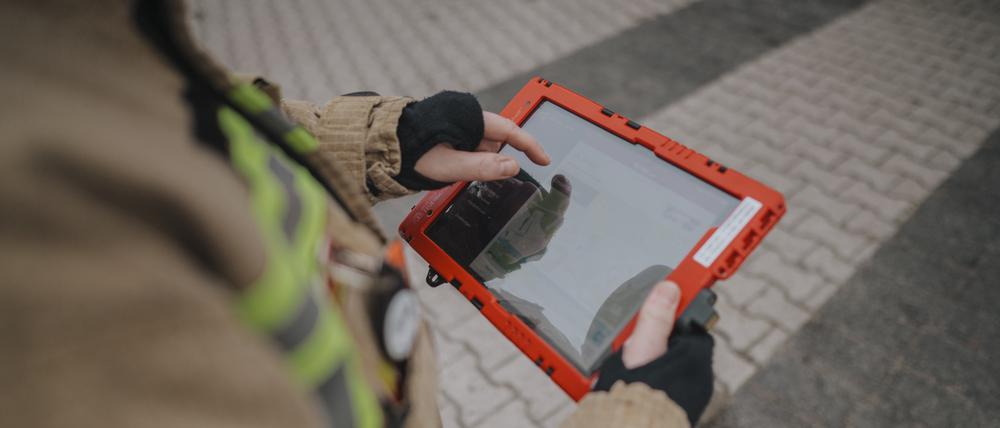Eine Einsatzkraft der Feuerwehr hält ein Tablet in der Hand.