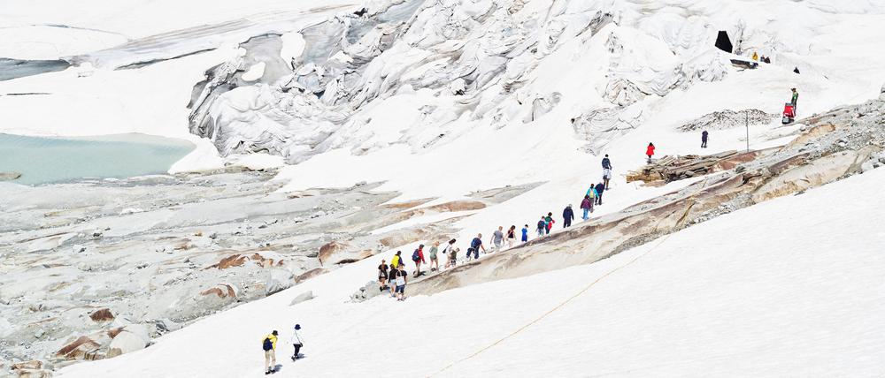 Touristen auf dem Weg zur künstlich ins Eis gehauenen Gletschergrotte, Rhonegletscher, Schweiz, 2019