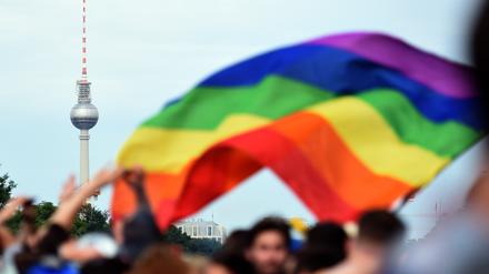 Eine Regenbogenflagge weht über einer Menschenmenge, im Hintergrund ist der Berliner Fernsehturm zu sehen. (Symbolbild)