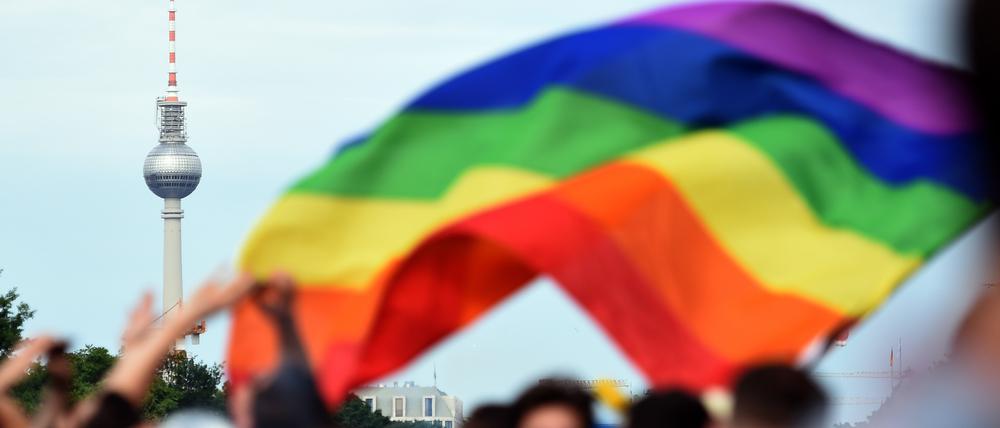 Eine Regenbogenflagge weht über einer Menschenmenge, im Hintergrund ist der Berliner Fernsehturm zu sehen. (Symbolbild)