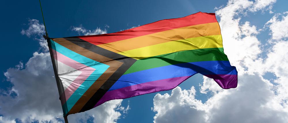 Eine Pride-Flagge weht vor Wolken im Wind.